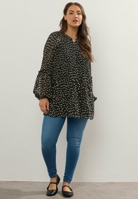 Svart genomskinlig blus med vita prickar, plisserad design och vida ärmar. Matchad med blå tajta jeans och svarta ballerina.