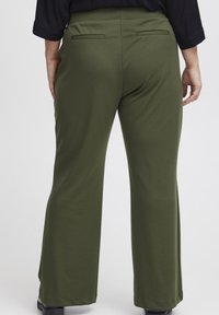 Gröna, vida byxor i mjukt tyg, med två bakfickor och en slät yta. Inga synliga knäppningar eller dekorationer.