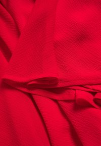 Tissu rouge texturé avec un motif fripé, présentant des plis et des rouleaux superposés, créant une apparence douce et drapée.