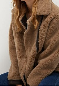 Brązowa polarowa kurtka z zamkiem z przodu, dużym kołnierzem i strukturalną powierzchnią. Posiada kontrastowe podszycie i luźny krój.