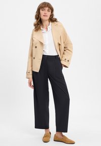 Beige, doppelt geknöpfter Blazer, weißes Hemd mit Kragen, schwarze weit geschnittene Hosen und braune Slipper, mit glatten Texturen und minimalistischem Akzent.