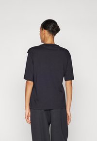 Schwarzes Kurzarm-T-Shirt mit Rundhalsausschnitt, aus Baumwolle gefertigt. Es hat eine glatte Textur und wird mit dunklen Hosen kombiniert.