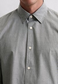 Chemise à rayures grises avec un col classique, des boutons blancs et une coupe décontractée, fabriquée en tissu léger en coton mélangé.