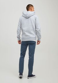 Grå hættetrøje med snor i hætten, parret med blå slim-fit bukser og marineblå lavtop sneakers. Glat stof, afslappet design.
