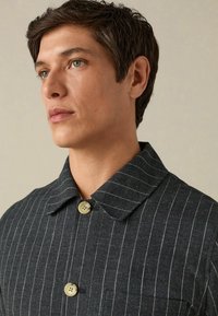 Tamno sivi prugasti sako sa zaobljenim ovratnikom, dva dugmeta i džepom na prsima. Tkanina ima teksturiranu završnicu.