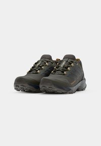 Groene buitenschoenen met een getextureerde bovenkant, rubberen zool en versterkte neus. Voorzien van bruine veters en zwarte accenten aan de zijkanten.