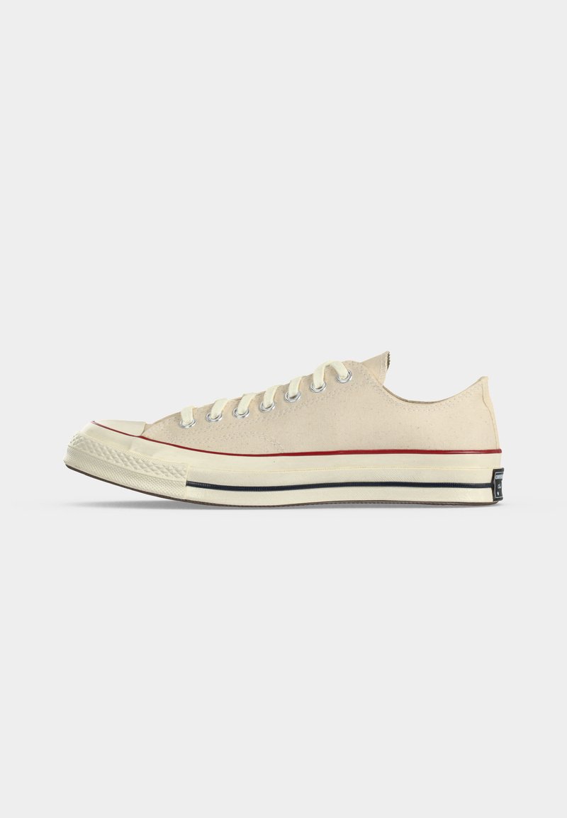 Sneaker beige in tela a taglio basso con suola in gomma bianca, strisce rosse e nere e lacci bianchi, mostrata dal lato esterno.