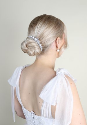 Abito bianco con maniche a fiocco trasparenti, dettagli in perline e una schiena elegante. Capelli raccolti in uno chignon basso con un accessorio floreale argento.