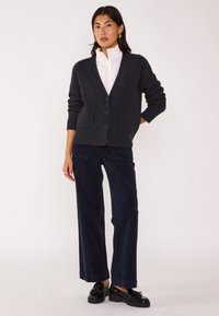 Cardigan blu navy con texture a coste, scollatura a V e chiusura con bottoni. Abbinato a pantaloni in corda blu navy a gamba larga e mocassini neri.