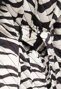 Ύφασμα μαύρο-άσπρο με ρίγες ζέβρας, καπιτονέ, με εμφανείς ραφές και μαζεμένες πτυχώσεις που δημιουργούν υφή και βάθος.