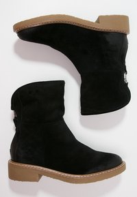 Bottines noires en daim avec un bout rond, une semelle plateforme marron basse et un détail de fermeture éclair sur le côté. Texture lisse avec des accents de couture.