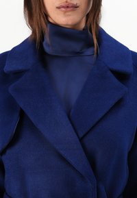 Navy blue wool blend coat with wide lapels and a soft texture, worn over a matching high-neck top, showcasing a cohesive design.