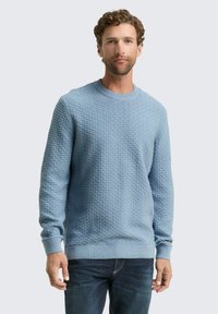 Lichtblauwe gebreide trui met een gestructureerd patroon, ronde halslijn en geribde manchetten en zoom. Gekocht met donkere jeans.