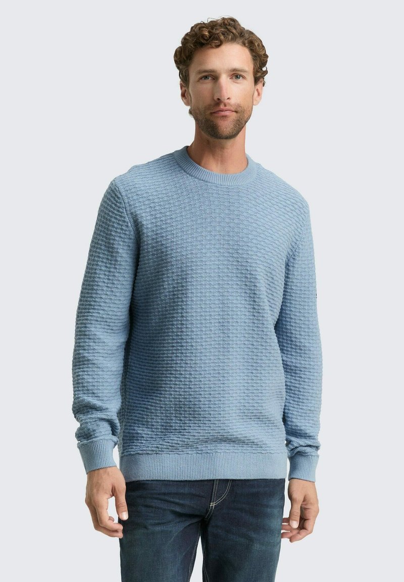 Lichtblauwe gebreide trui met een gestructureerd patroon, ronde halslijn en geribde manchetten en zoom. Gekocht met donkere jeans.