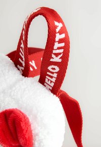 Vit plyschväska med en mjuk, fluffig textur, med röda tyghandtag med texten "HELLO KITTY". Rund form med en rundad rosa accent.