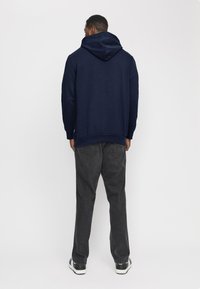Felpa blu navy con cappuccio regolabile, tessuto testurizzato e polsini a coste; abbinata a jeans grigi scuri e sneakers nere.