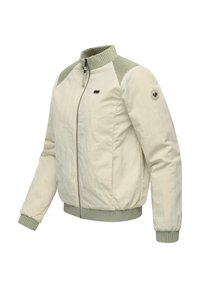 Veste beige clair zippée avec col, poignets et ourlet côtelés en vert doux, avec un petit badge logo sur la manche gauche.
