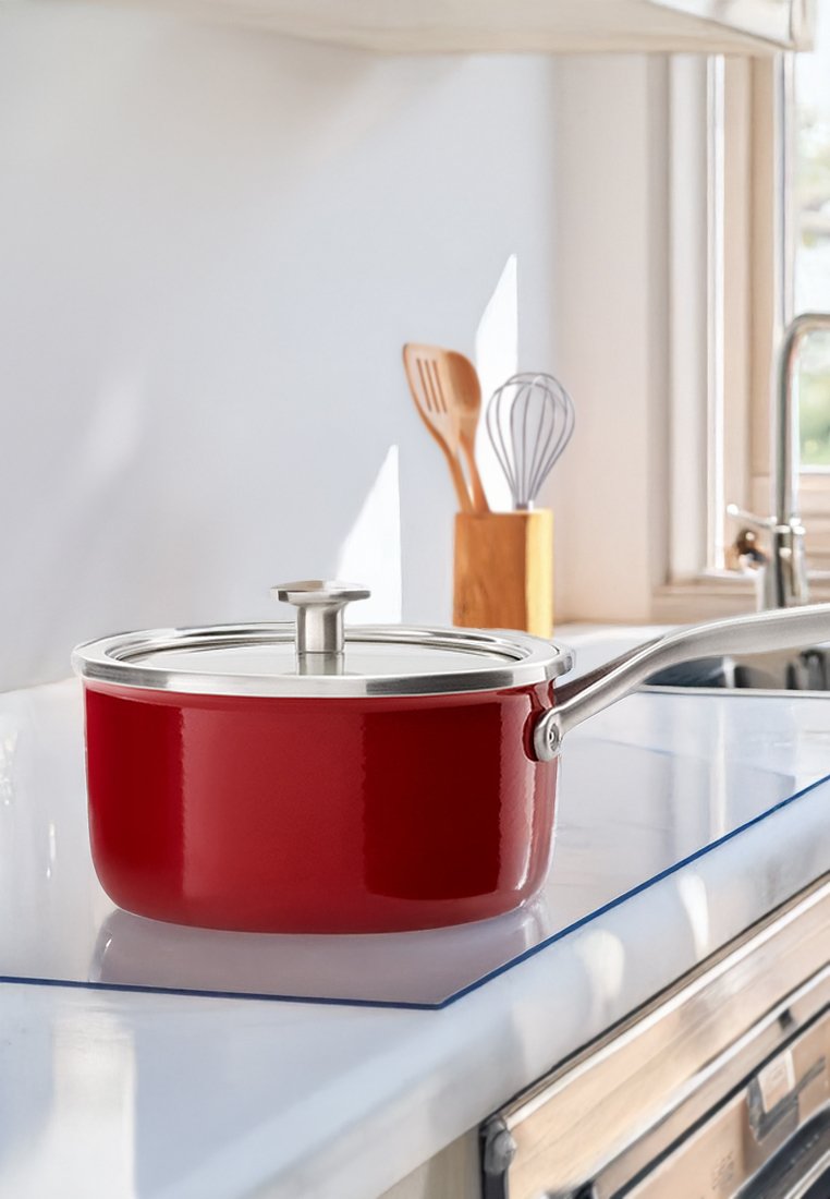 Casserole rouge avec un couvercle et une poignée en acier inoxydable. Fini lisse et brillant, de forme ronde, placée sur un comptoir blanc à côté d'ustensiles en bois.
