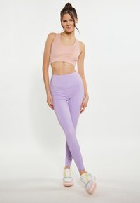 Világos rózsaszín crop top, amelyet magas derekú levendula színű leggingsszel párosítottak. A modellen színes sportcipők vannak. A sima, ruganyos anyagok és a testhez simuló forma jellemzi.