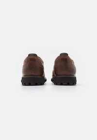 Zapatos de cuero marrón con un acabado texturizado, que presentan una suela de goma negra resistente, collar acolchado y detalles de costura en la parte trasera.