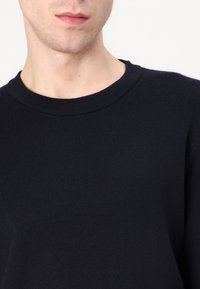 Dunkelblauer Strickpullover mit glatter Textur und geripptem Rundhalsausschnitt. Der Stoff wirkt weich und eignet sich gut für legere Outfits.