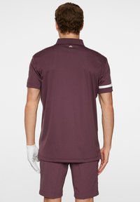 Lyhythihainen, burgundy golfpaita, jossa on kaulus, ja jossa on kontrastivärinen valkoinen raita hihoissa sekä logotieto takana.