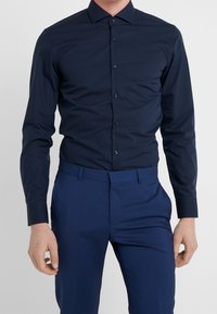 Marineblauw shirt met lange mouwen, een spreidkraag, knoopsluiting en een getailleerd ontwerp. Gecombineerd met bijpassende donkerblauwe broek.