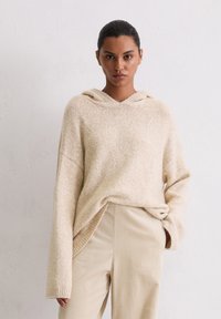 Hoodie en tricot beige avec une finition texturée, coupe oversize et manches larges. Assorti à un pantalon côtelé beige clair avec des poches latérales.