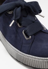 Zapatilla de ante azul marino con suela texturizada gris, ojetes metálicos y grueso detalle en los cordones. Punta redondeada y diseño de perfil bajo.