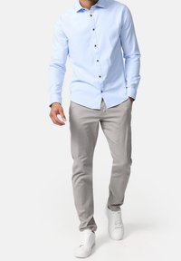 Lichtblauw overhemd met lange mouwen en knopen in een donkere tint, gecombineerd met grijze broek en witte sneakers. Soepele stof en een getailleerde pasvorm.