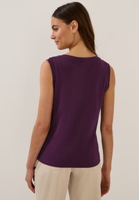 Top viola senza maniche con scollo rotondo, texture liscia e silhouette aderente, abbinato a pantaloni chiari. Design minimal.