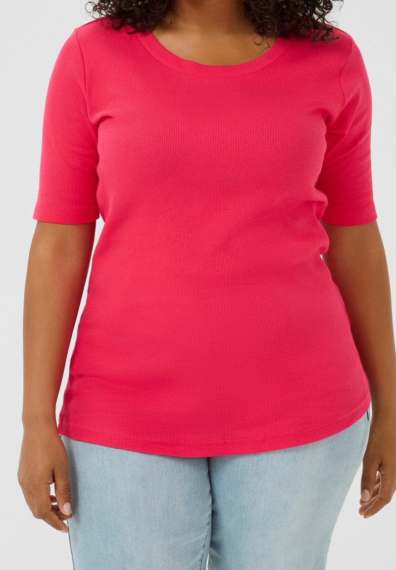 Femme portant un haut à manches courtes côtelé rose vif et un jean en denim bleu clair, visible des épaules aux hanches.