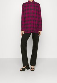 Fuchsiarutigt knappat skjorta med långa ärmar, ihop med svarta raka byxor och svarta klacksandaler. Har en framficka.