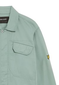 Lichtgroene jacket gemaakt van gladde stof, met een knoopsluiting, twee borstzakken en een geborduurd geel logo op de mouw.