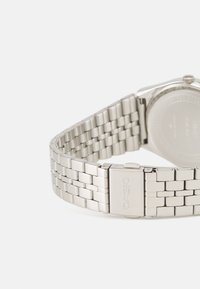 Silverfärgad rostfri stålarmband med länkdesign, försett med lås. Klockan har ett polerat metallfinish.