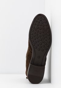 Chaussure en daim marron présentée semelle vers l'avant, avec un motif circulaire antidérapant en caoutchouc texturé, un talon et une tige en cuir cousu.