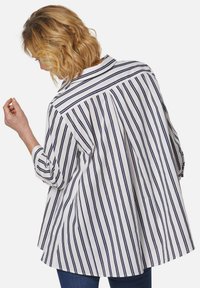 Weißes Hemd mit vertikalen marineblauen Streifen, ausgestattet mit einer Rückenpasse, ausgestelltem Schnitt und umgeschlagenen Ärmeln. Leichtes Gewebe mit einer weichen Textur.