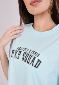 Camiseta de algodón azul claro con un atrevido estampado gráfico en blanco y negro que dice "PROJECT X PARIS PXP SQUAD" con detalles bordados.