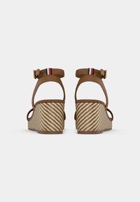Brown wedge sandals with a striped ankle strap and zigzag patterned woven base, featuring cut-out side design and gold buckle accent.