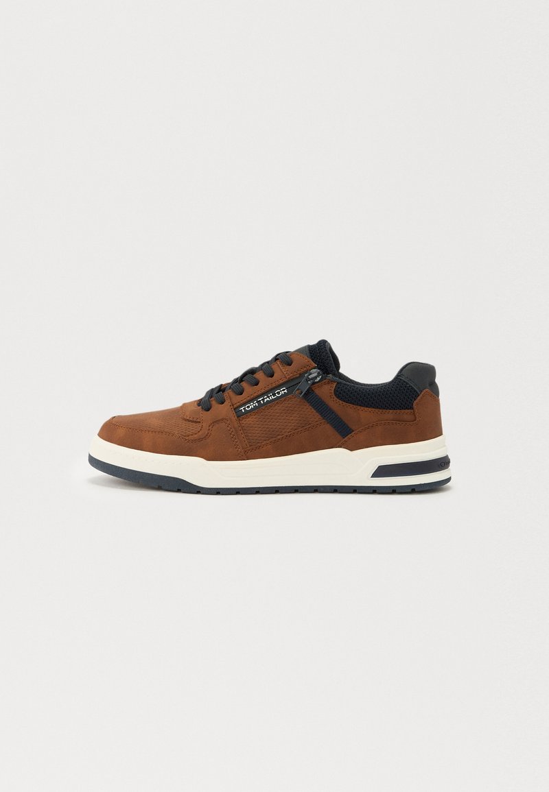 Barna velúr sneaker textil kiemelésekkel, fekete fűzőkkel, fehér középtalppal és textúrázott talppal. Oldalán logós részlet található.