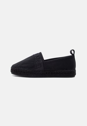 Svart slip-on espadrille med vevd såle, stoffoverdel og trekkfane ved hælen, med subtil preget logo på toppen.