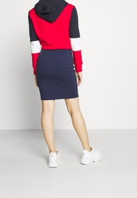 Röd, marinblå och vit färgblockerad hoodie med huva, tillsammans med en marinblå slim-fit kjol med sidodetaljer; bärs med vita sneakers.