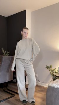 Beige oversized sweatshirt en bijpassende wijde broek in een zachte, getextureerde stof. Gestyled met donkergroene slip-on schoenen. Indoor omgeving.