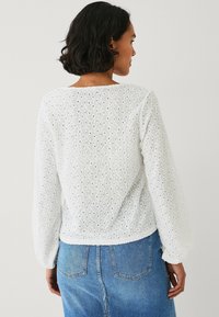 Blusa bianca con un motivo a occhio di pernice testurizzato, maniche lunghe a sbuffo e vestibilità rilassata, abbinata a jeans in denim blu.