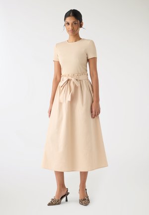 Donna che indossa un top beige a maniche corte e una gonna midi a vita alta abbinata con cintura annodata, abbinata a scarpe con tacco leopardate.