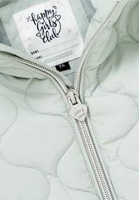 Giacca trapuntata verde chiaro con motivo a scallop, zip argentata e tirazip a forma di cuore inciso "Little & Loved". Etichetta visibile all'interno.