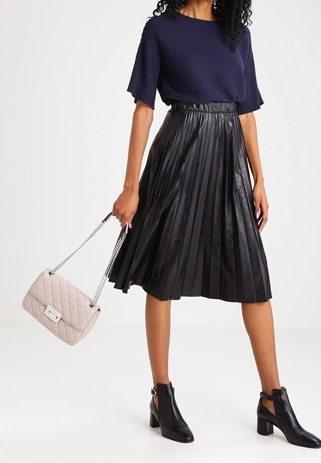 Top a coste navy, gonna midi plissettata nera, stivali neri alla caviglia e borsa a tracolla trapuntata beige chiaro con catena argentata.