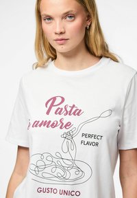 Camiseta de algodón blanca con un diseño gráfico que presenta un arte lineal negro de pasta y texto rojo que dice "Pasta è amore" y "Sabor Perfecto".