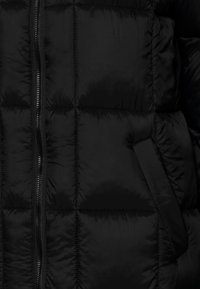 Zwarte donzen jas met doorgestikte delen, een centrale rits en een zijzak. Het materiaal heeft een gladde, glanzende textuur.