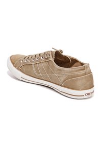 Zapatillas de lona beige con costuras blancas, punta redondeada y suela de goma. Presentan un diseño de cordones y un acento de marca en el talón.